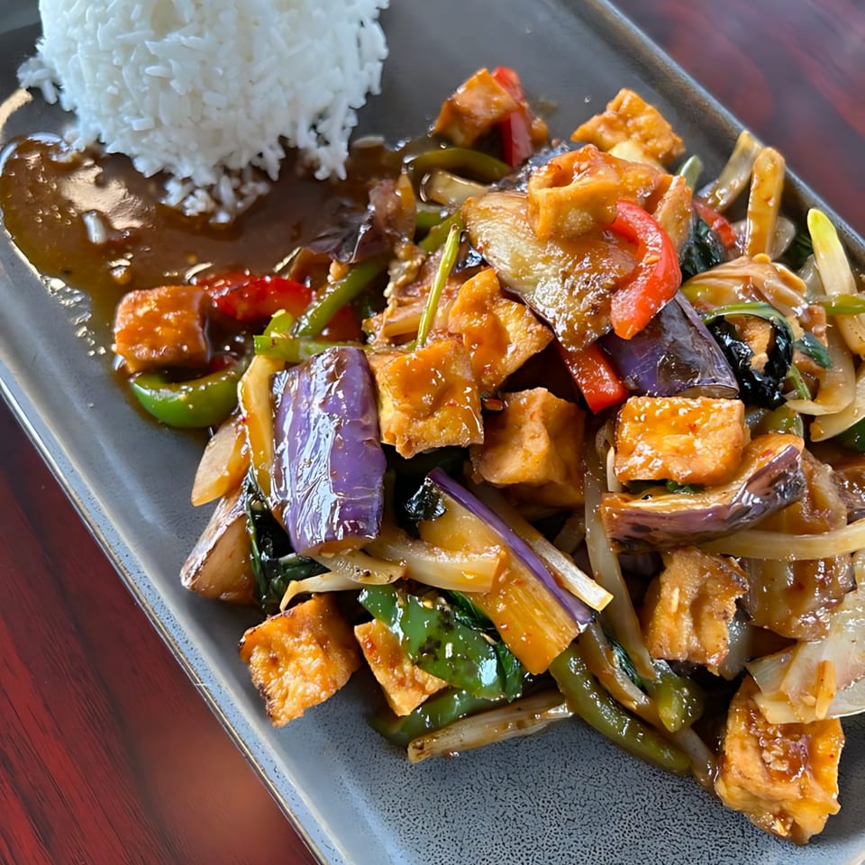 Thai stir-fried tofu with eggplant, bell peppers, and onions, served with white rice.