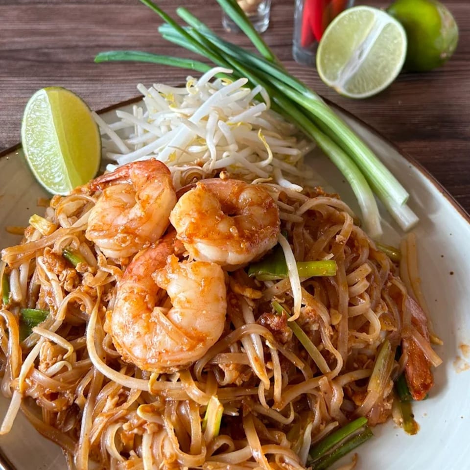 Shrimp Pad Thai with bean sprouts, green onions, and lime wedges on a white plate.