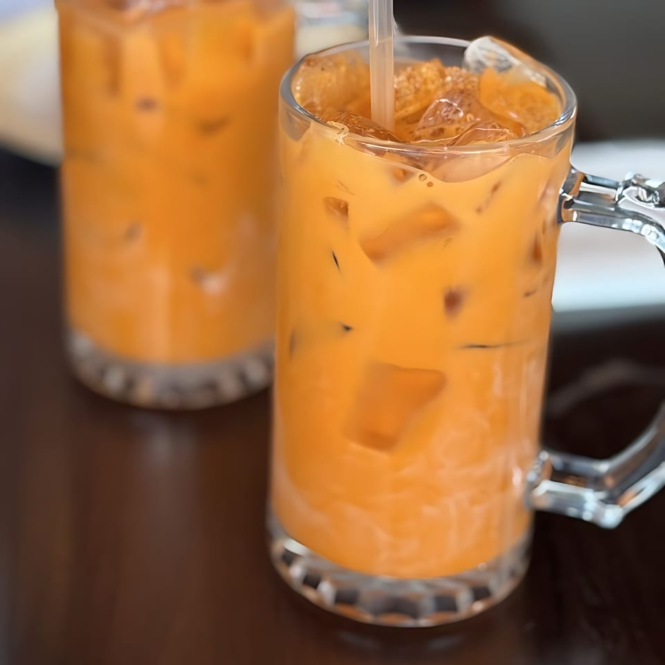 Two glasses of iced Thai tea with straws on a dark table at Monkey Thai Diner.