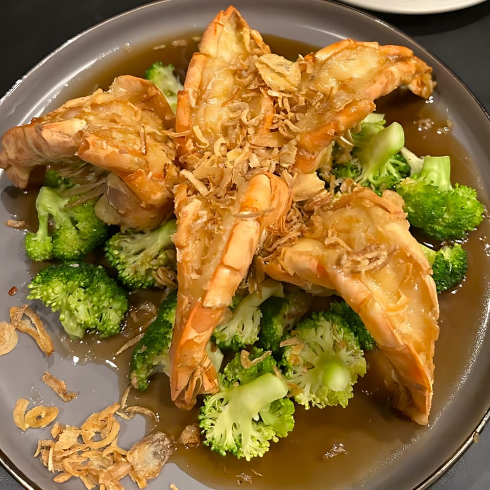 Thai dish with large prawns, broccoli, and crispy fried garlic in a savory brown sauce.