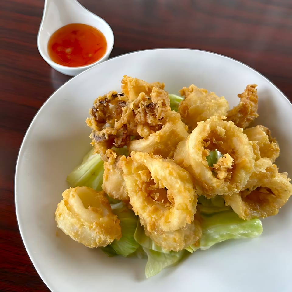 Crispy fried calamari rings and tentacles on lettuce, with a side of sweet chili sauce.