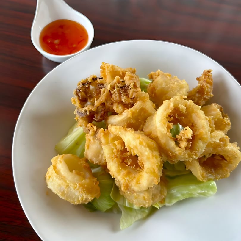 Crispy fried calamari rings and tentacles on lettuce, with a side of sweet chili sauce.