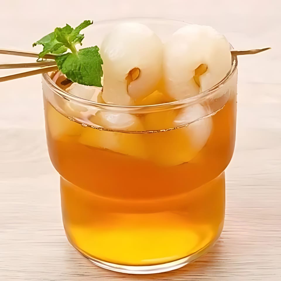 Lychee iced tea with mint and lychee fruit on a skewer, a refreshing Thai drink.