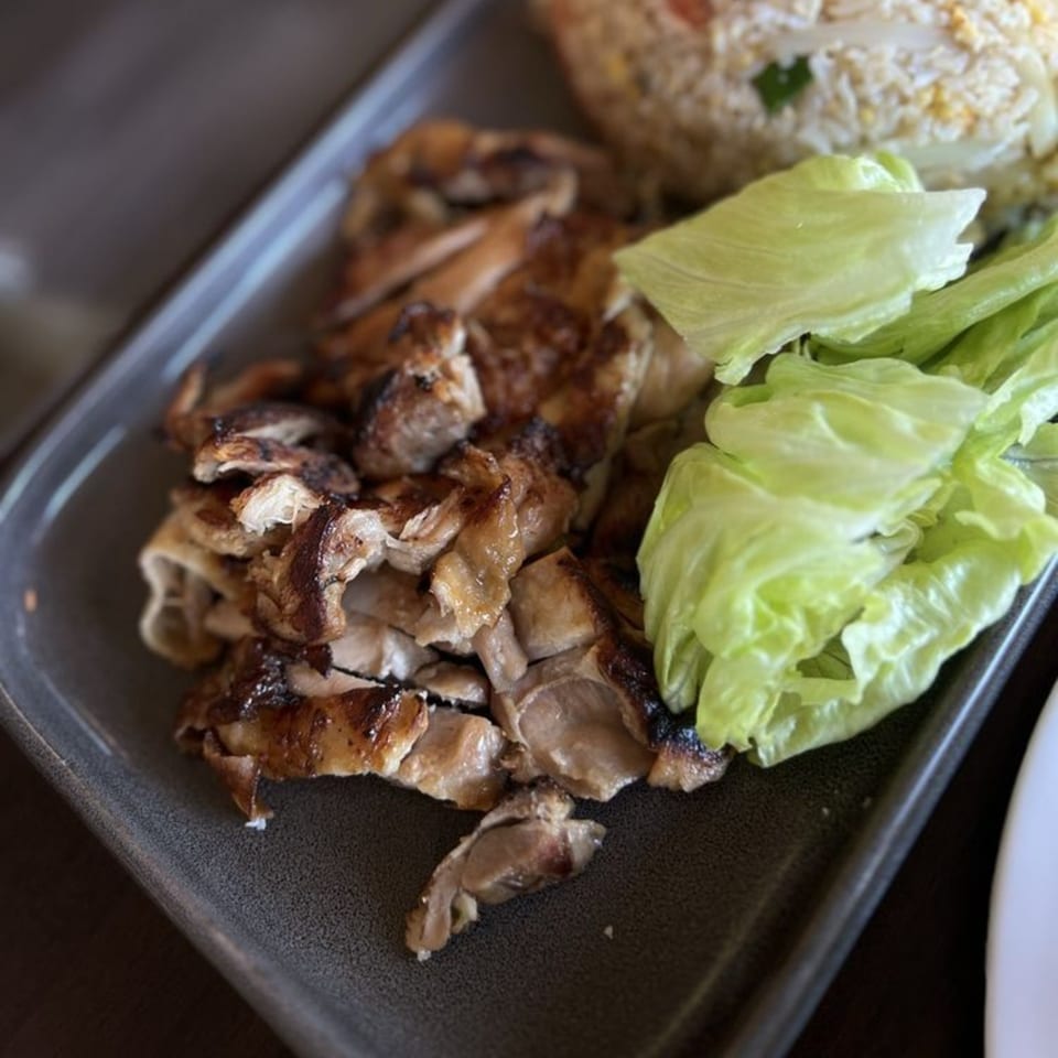 Grilled chicken pieces, fresh lettuce, and fried rice on a dark gray plate.
