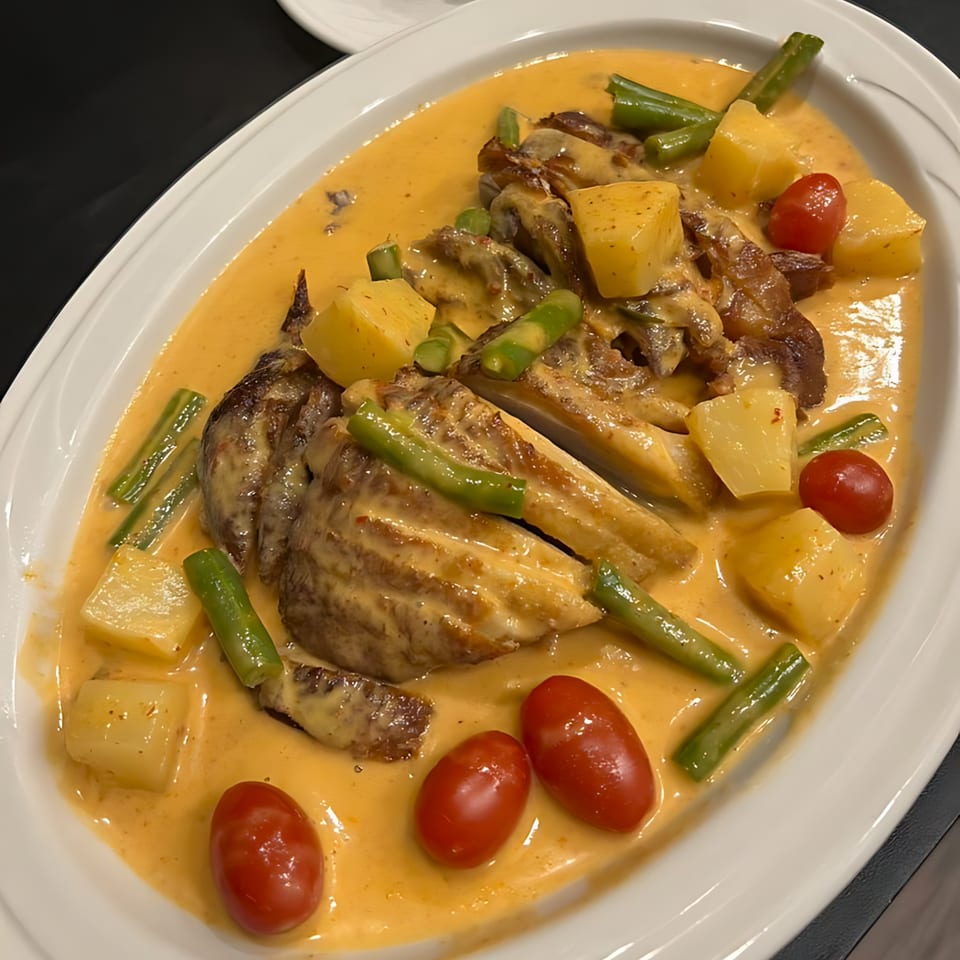Thai red curry with roasted duck, pineapple, cherry tomatoes, and green beans on a white platter.