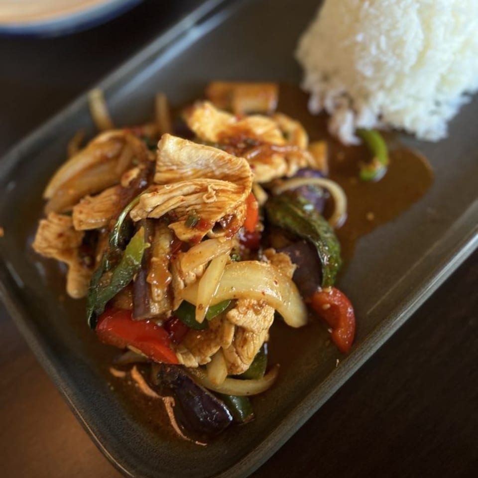 Thai stir-fried chicken with vegetables and rice on a dark rectangular plate.